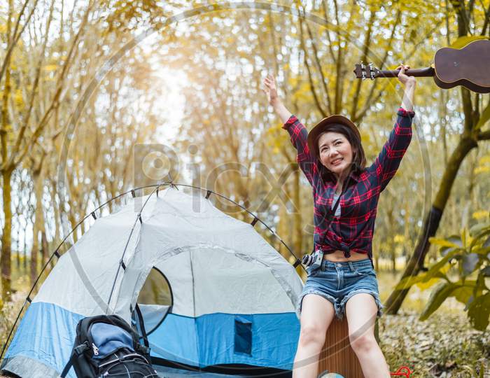 Beauty Asian Woman Holding Guitar And Raising Hands In Forest. Pine Woods Background. People And Lifestyles Concet. Camping And Travel Concept