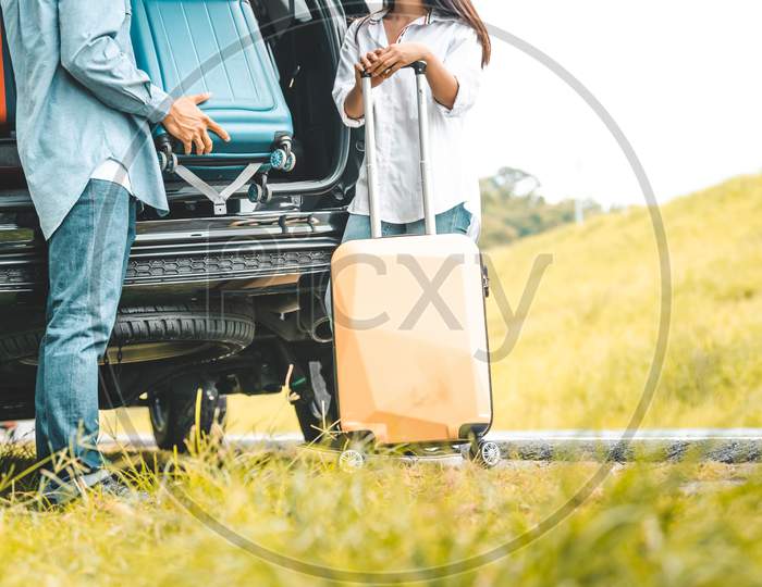 Closeup Lower Body Of Couple Lift Down Trolly Luggage At Back Of Suv Car Trunk Along Road Trip With Autumn Mountain Hill Background. Freedom Friend Road Way. Two People Lifestyle Transportation Travel