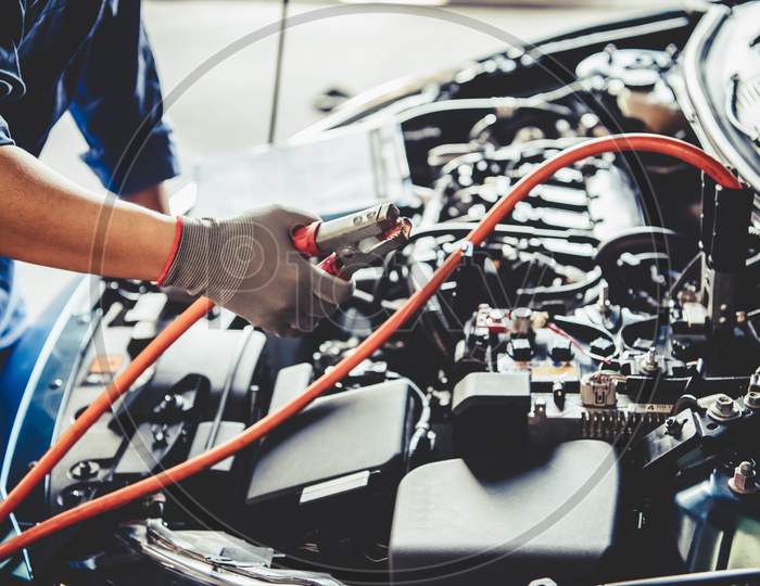 Car Mechanic Holding Battery Electricity Trough Cables Jumper And Checking To Maintenance Vehicle By Customer Claim Order In Auto Repair Shop Garage. Repair Service. People Occupation And Business Job