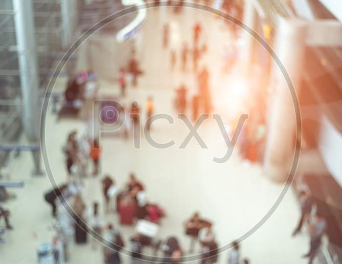 Blurry Background Of Airport Terminal And Convention Hall With Crowd People. Orange Sun Light Element. Business And Travel Concept. Abstract Background Theme.