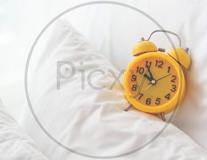 Yellow Alarm Clock On White Bed Background. Travel And Vacation Concept. Home Object Accessories Theme.