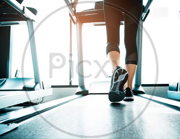 Close Up Of People Who Exercising On Treadmill. Close-Up Of Woman Legs Walking By Treadmill In Sports Club. Fitness And Body Build Up Concept. Workout And Strength Training Concept. Sport Club Theme.