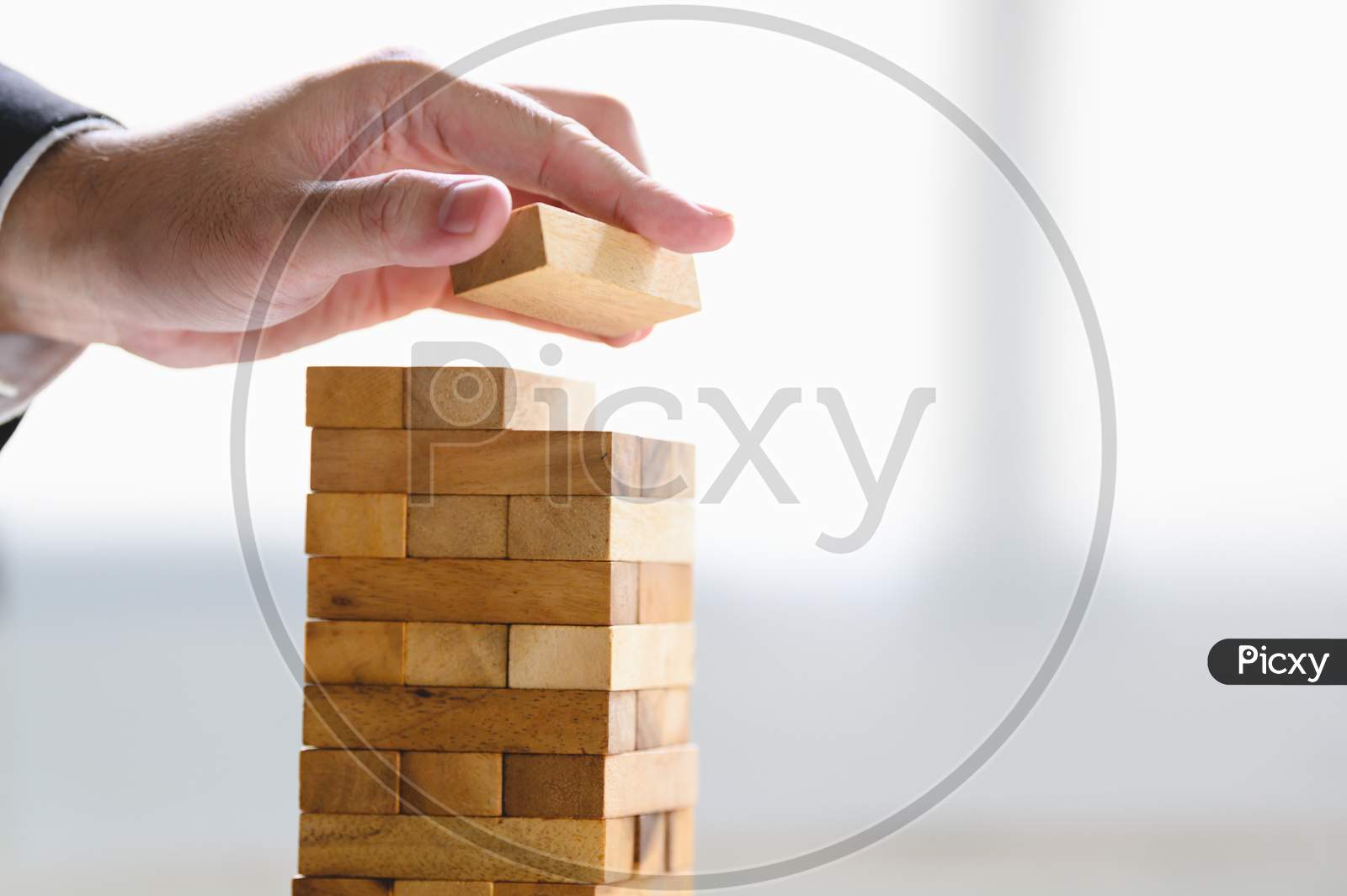 Businessman Arranging Wood Block And Stacking As Tower By Hand. Business Organization And Company Growth Progress. Success Of Strategy And Money Investment Concept. Risk Management Project Theme