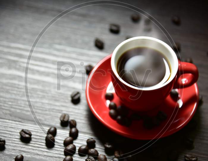 Red Cup Coffee With Stream Vapor And Coffee Bean On Wood Table, Selective Focus On Edge Of Cup, Drinking Concept