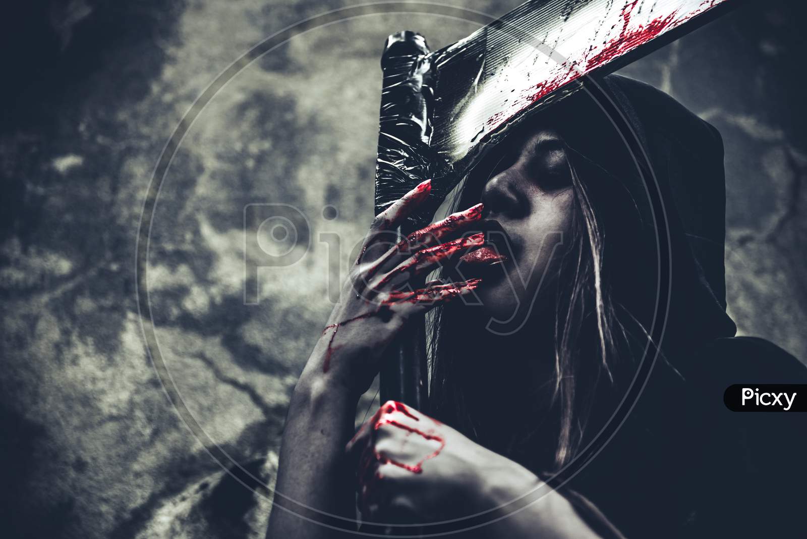 Witch Licking Blood On Fingers. Female Demon Angel In Black Clothes And Hood On Grunge Wall Background. Halloween Day And Mystery Concept. Fantasy Of Magic Theme. Afterlife And Death Concept.