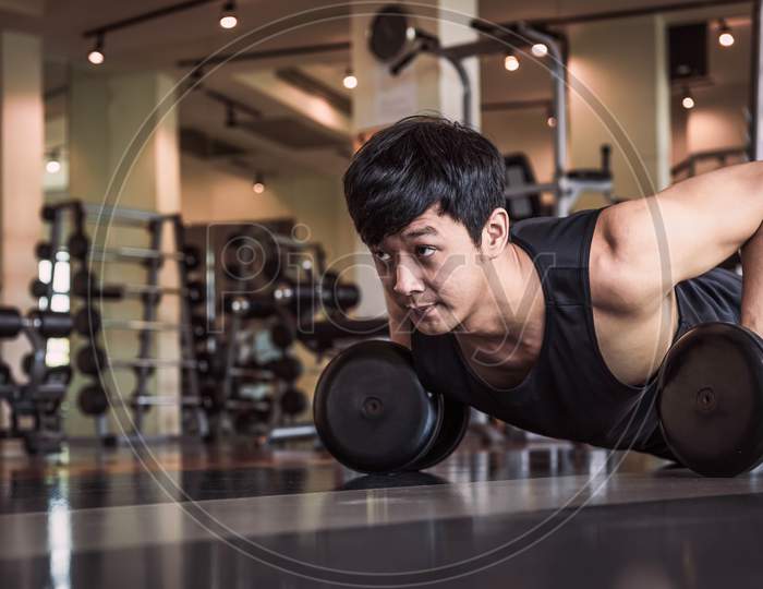 Portrait Of Asian Fitness Man Doing Pushing Up Exercise With Dumbbell In Gym. People Lifestyle And Sport Concept. Sportsman Holding Weight By Two Hands On Floor.