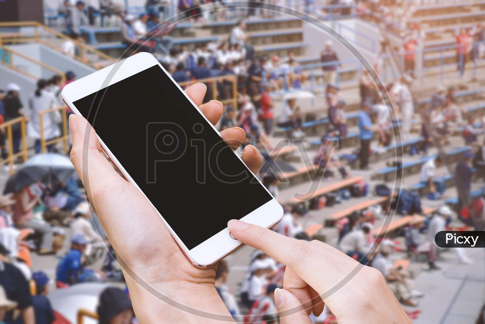 Woman Hold Smart Phone And Touch Button By Hand With Blank Screen For Advertisement, Stadium And Audiences Background ,Technology And Sport Concept