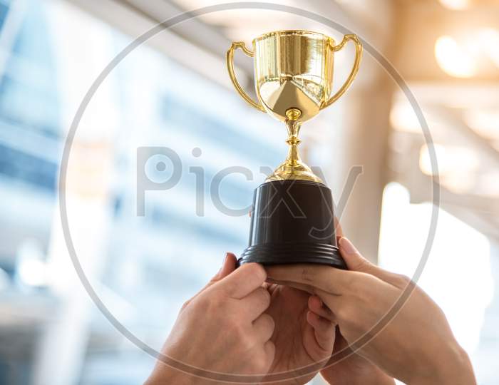 Champion Golden Trophy For Winner With Sport Player Hands In Sport Stadium Background. Success And Achievement Concept. Sport And Cup Award Theme. American Football Award And Match Game Play Prize