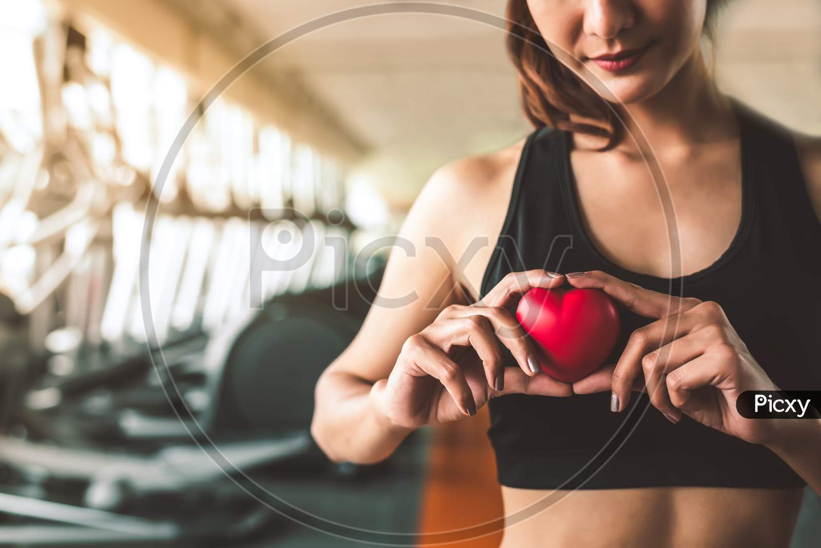 Happy Sport Woman Holding Red Heart In Fitness Gym Club. Medical Cadio Heart Strength Training Lifestyle. Pretty Female Sport Girl Workout Exercise. Cardiac Healthy And Wellbeing. Massage Ball In Hand