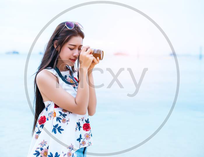 Asian Woman Enjoy Take Photo By Digital Camera At Beach. Single And Lonely Woman Concept. Happiness And Lifestyle Concept. Beauty And Nature Theme. Ocean And Sea Background. Technology And Woman Day