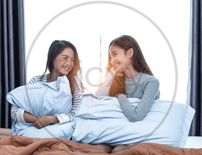Two Asian Lesbian Women Looking Together In Bedroom. Couple People And Beauty Concept. Happy Lifestyles And Home Sweet Home Theme. Cushion Pillow Element And Window Background.