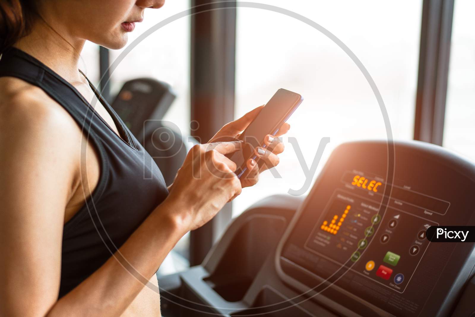 Woman Using Smart Phone When Workout Or Strength Training At Fitness Gym On Treadmill. Relax And Technology Concept. Sports Exercise And Health Care Theme. Happy People And Comfortable Application