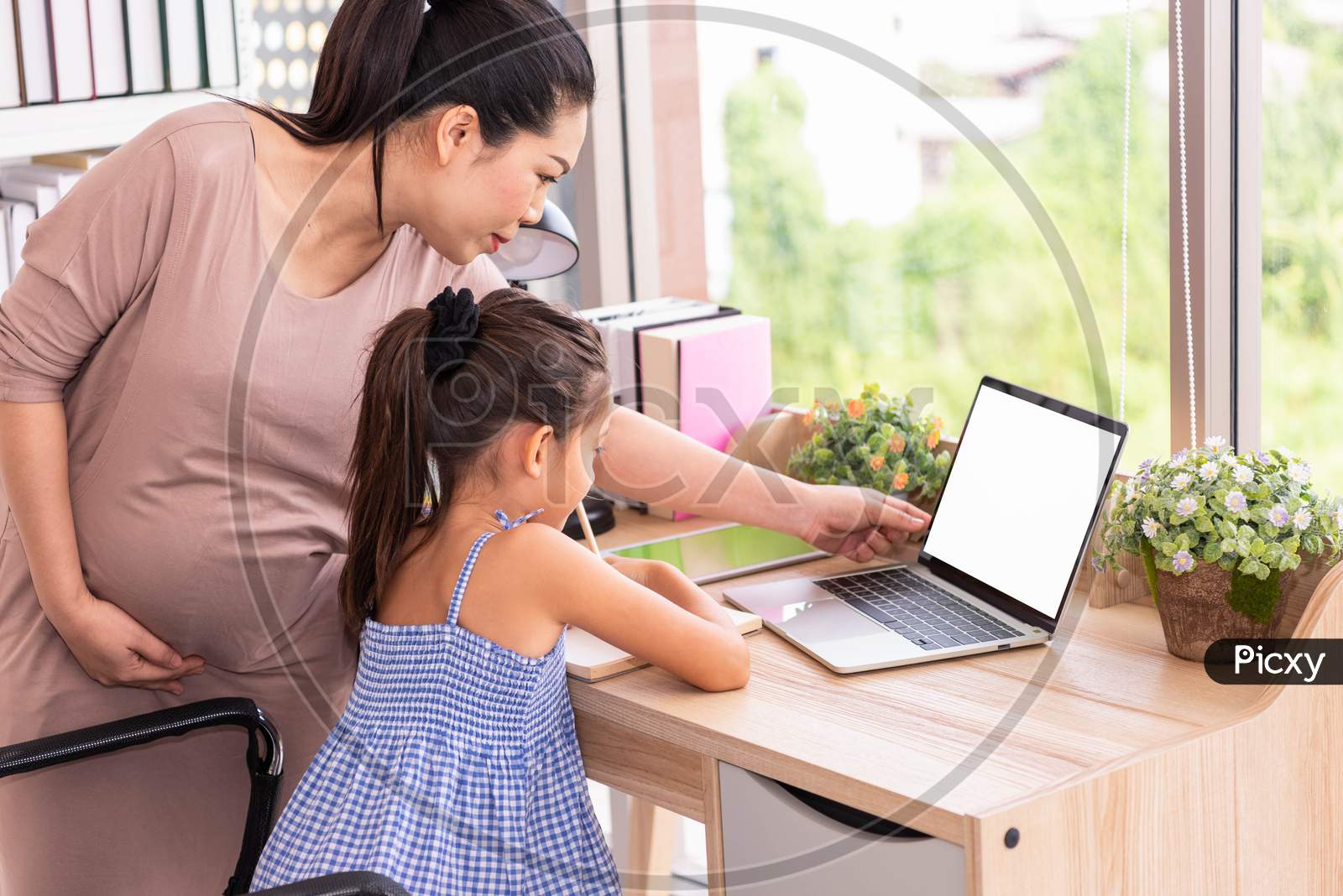 Cute Daughter And Her Pregnant Mother Using White Blank Screen Laptop At Home. Parenthood And Technology. Health And Medical. People Lifestyles And Family Concept. Copy Space