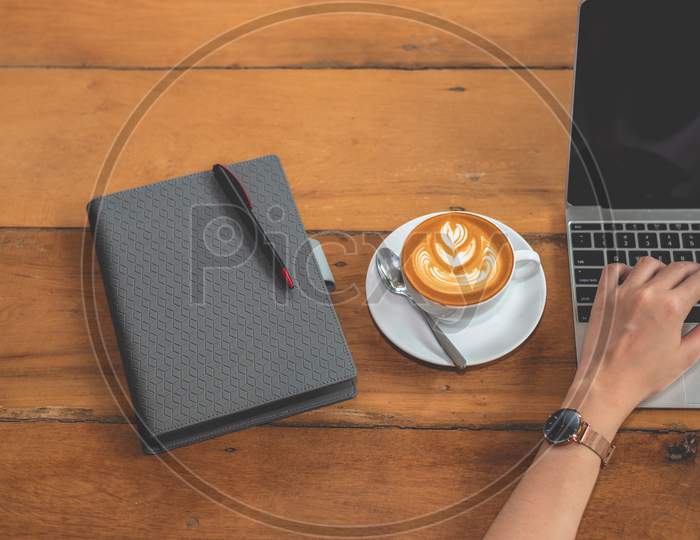 Top View Of Hand Of Woman Using Laptop Computer With Notebook And Coffee Cup. People And Drinks And Technology Concept. Working Woman Theme.