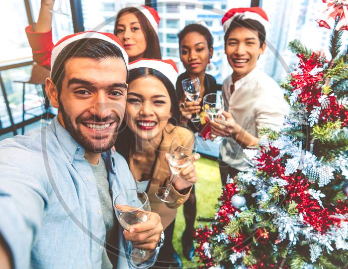 Working People Self Portrait Of Mixed Race Friends Celebrating For Merry Christmas And Happy New Year Party 2020 In Working Office. Multiracial Diversity Young Business Group Selfie By Phone Camera