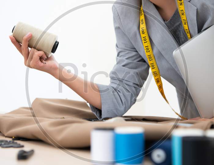 Closeup Of Dressmaker Hand Holding Spool Of Thread Stylist Designer In Business Owner Workshop. Tailor And Sewing Concept. Portrait Of Happy Casual Trendy Fashion Designer Businesswoman In Studio
