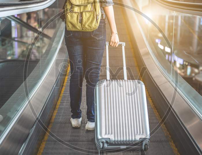 Back View Of Beauty Woman Traveling And Holding Suitcase On Escalator In Airport. People And Lifestyles Concept. Travel Around The World Theme. Adventure And Business Trip Theme.