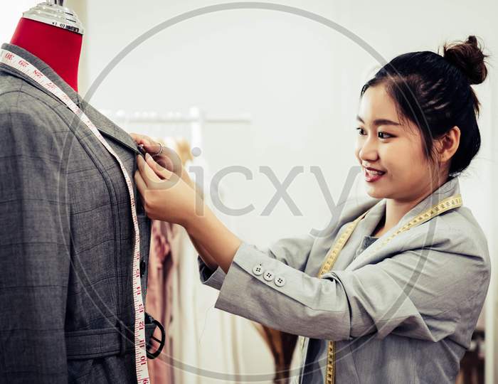 Asian Female Fashion Designer Girl Making Fit On The Formal Suit Uniform Clothes On Mannequin Model. Fashion Designer Stylish Showroom. Sewing And Tailor Concept. Creative Dressmaker Stylist.