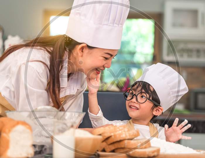 Cute Little Asian Boy Painting Beautiful Woman Face With Dough Flour. Chef Team Playing And Baking Bakery In Home Kitchen Funny. Homemade Food And Bread. Education Teamwork And Learning Concept.