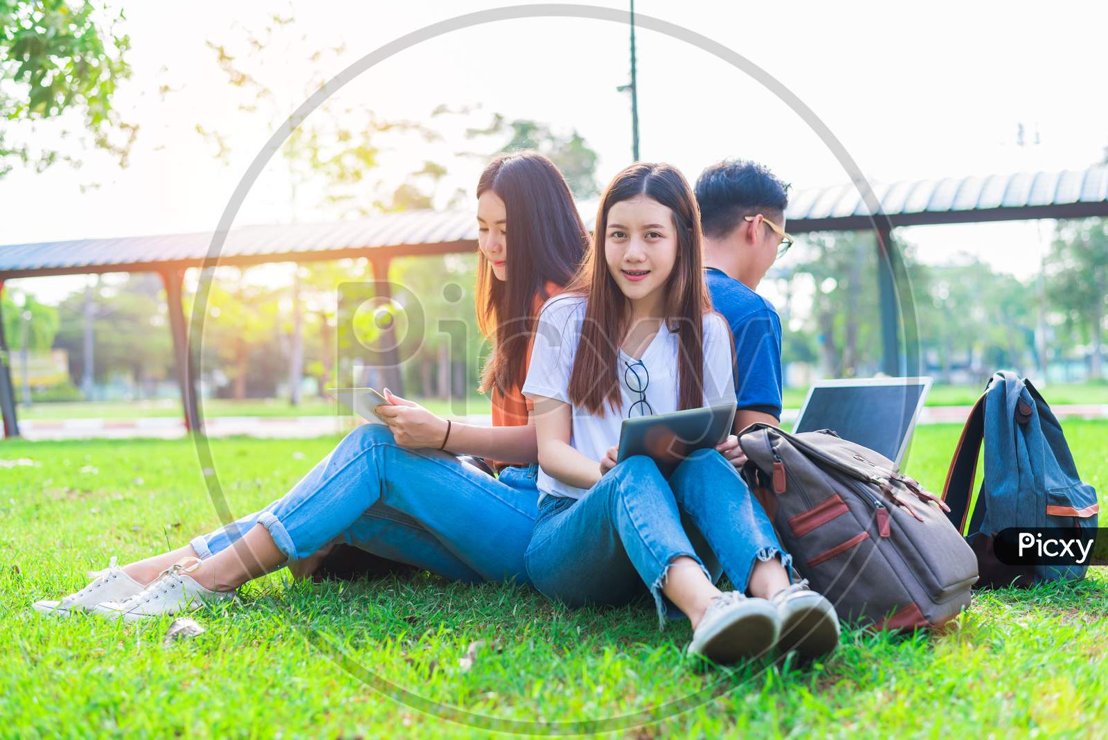 Group Of Asian College Student Using Tablet And Laptop On Grass Field At Outdoors. Technology And Education Learning Concept. Future Technology And Modern Entertainment Concept. Edutainment Theme.