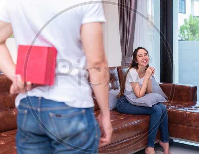 Boy Surprise His Asian Girlfriend By Holding Gift Box Behind Him At Their Home. Valentine'S Day And Pre Wedding Honeymoon Concept. People And Lifestyles Concept.