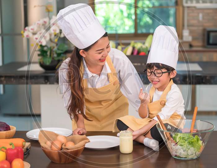 Happy Beautiful Asian Woman And Cute Little Boy With Eyeglasses Prepare To Cooking In Kitchen At Home. People And Family Concept. Homemade Food And Ingredients Concept. Two Thai People Lifestyles
