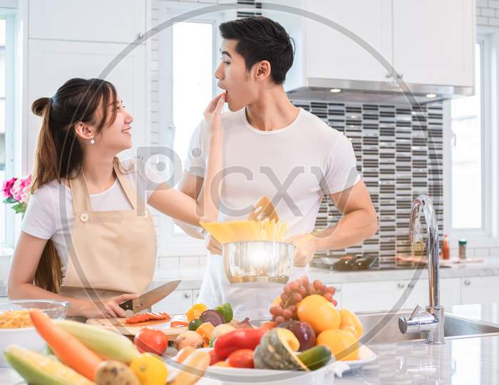 Asian Couples Feeding Food Together In Kitchen. People And Lifestyles Concept. Sweet Honeymoon And Holidays Concept. Valentines Day And Wedding Theme. Puppy Love And Romantic Theme.