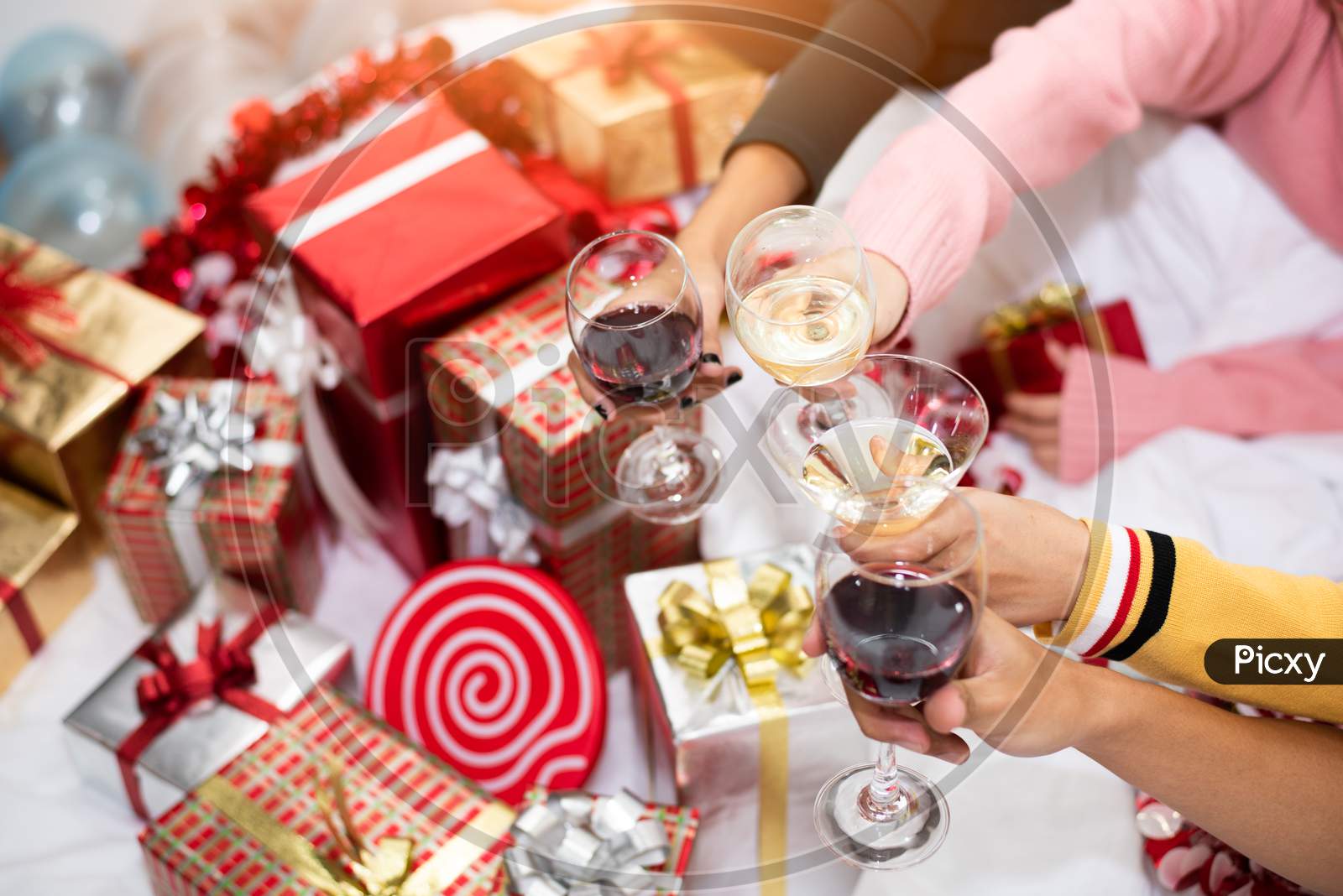 Hands Of People Celebrating New Year Party In Home With Wine Drinking Glasses And Present Background. New Year And Christmas Party Concept. Happiness And Friendship And Funny Together. Clinking Glass