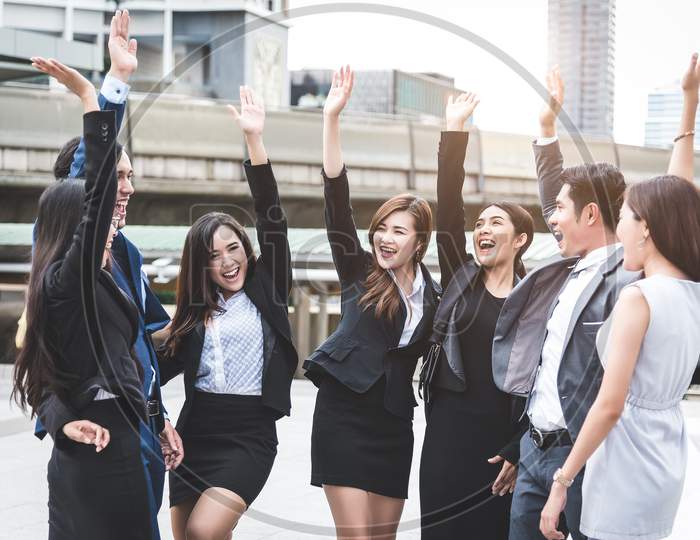 Portrait Of Successful Group Of Business People At Outdoor Urban. Happy Businessmen And Businesswomen Raising Hand As Team In Satisfaction Gesture. Successful Group Of People Smiling After Achievement