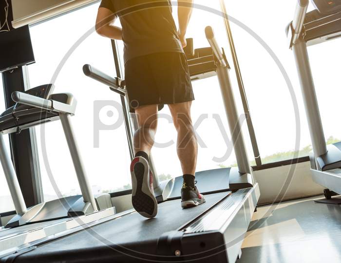 Legs Of Sportsman Running On Treadmill In Fitness Gym Center. Sport And Healthy Lifestyle Concept. People Workout And Exercise Activity. Back View Or Rear View