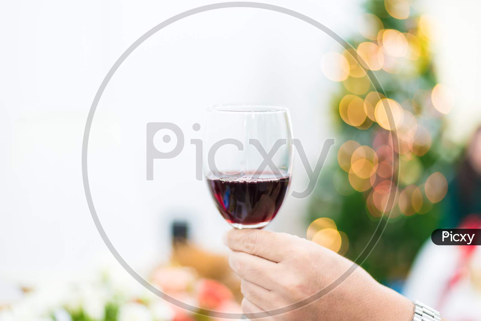 Glass Of Red Wine For Toasting In Party With Christmas Tree Background. Celebration And Anniversary Concept. New Year Toast And Drinking Concept.