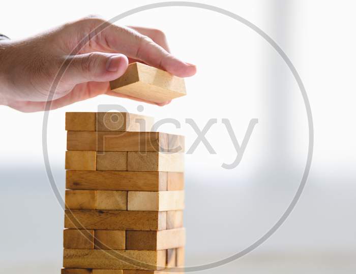 Businessman Arranging Wood Block And Stacking As Tower By Hand. Business Organization And Company Growth Progress. Success Of Strategy And Money Investment Concept. Risk Management Project Theme