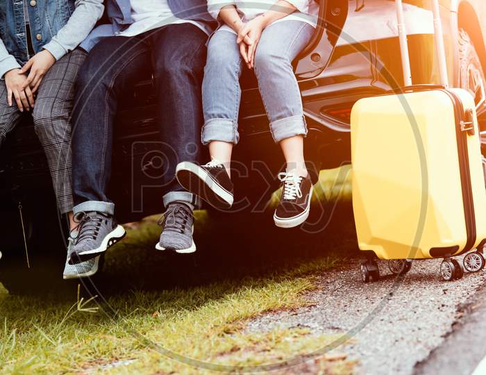 Closeup Lower Body Of Group Of Friends Relaxing On Suv Car Trunk With Trolly Luggage Along Road Trip With Autumn Mountain Hill Background. Freedom  Road Way. People Lifestyle Transportation Travel