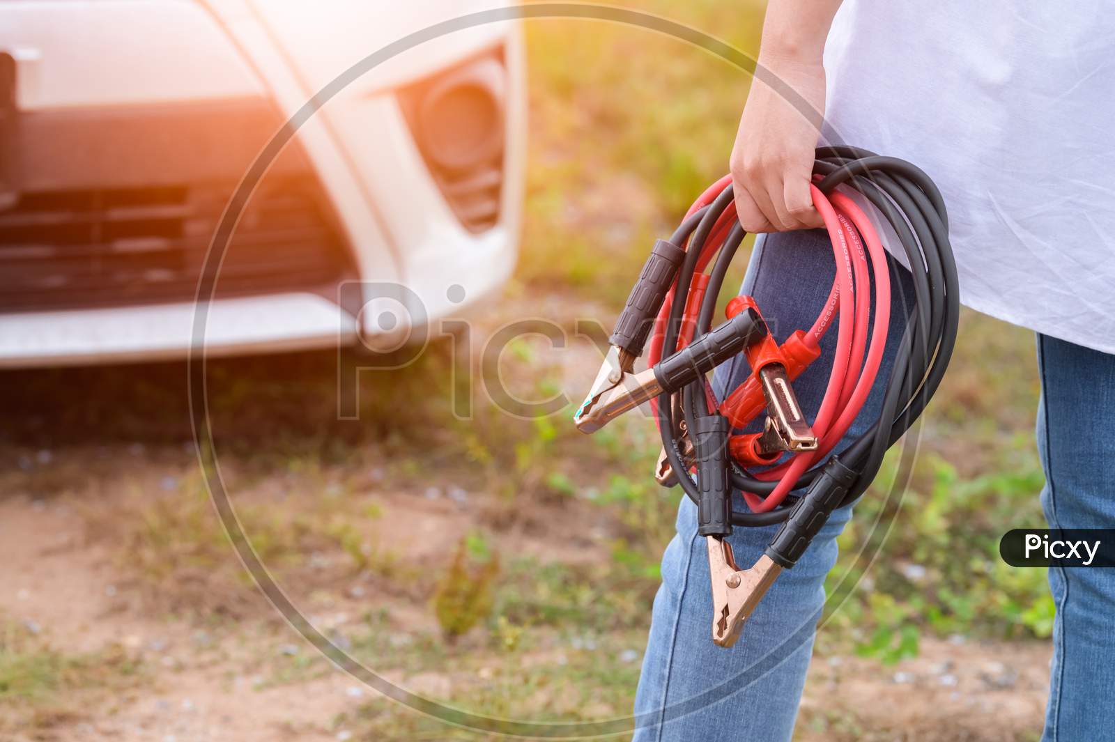 Closeup Of Woman Hand Holding Battery Cable Copper Wire For Repairing Broken Car By Connect Battery With Red And Black Line To Electric Terminal By Herself. Car Maintenance And Transportation Concept