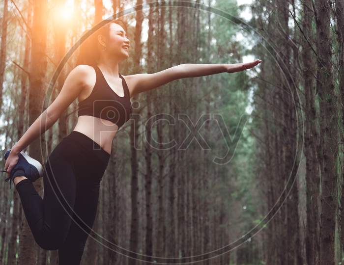 Beauty Asian Woman Doing Yoga And Stretching Legs Before Running In Forest At Outdoors. Sports And Nature Concept. Lifestyle And Activity Concept. Pine Woods Theme.