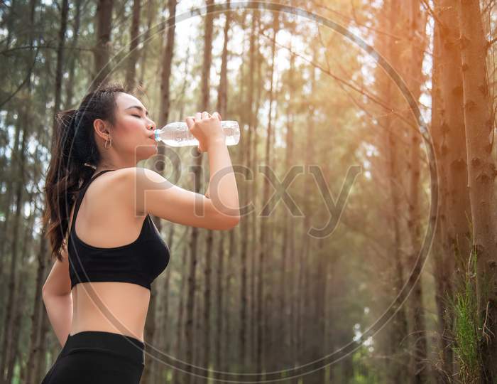 Asian Beauty Woman Drinking Water In Forest. Sport And Healthy Concept. Jogging And Running Concept. Relax And Take A Break Theme. Outdoors Activity Theme.