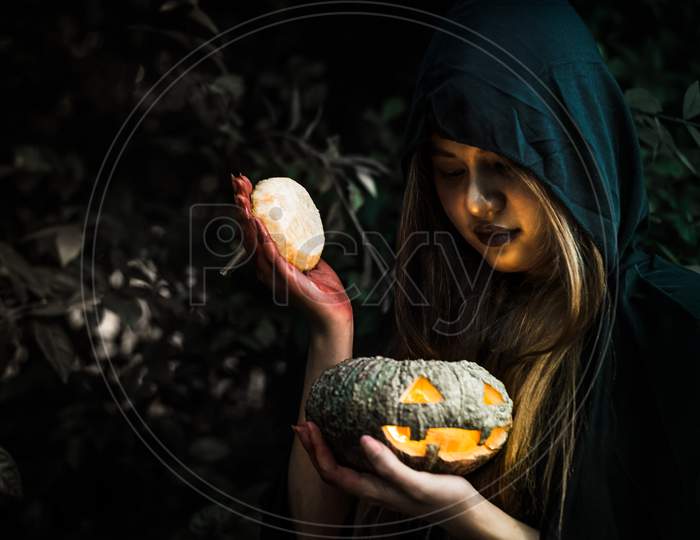 Witch Opening Pumpkin Lid By Hand. Old Woman Holding Bright Pumpkin In Dark Forest. Halloween Day And Mystery Concept. Fantasy Of Magic Theme. Demon Angle Theme.