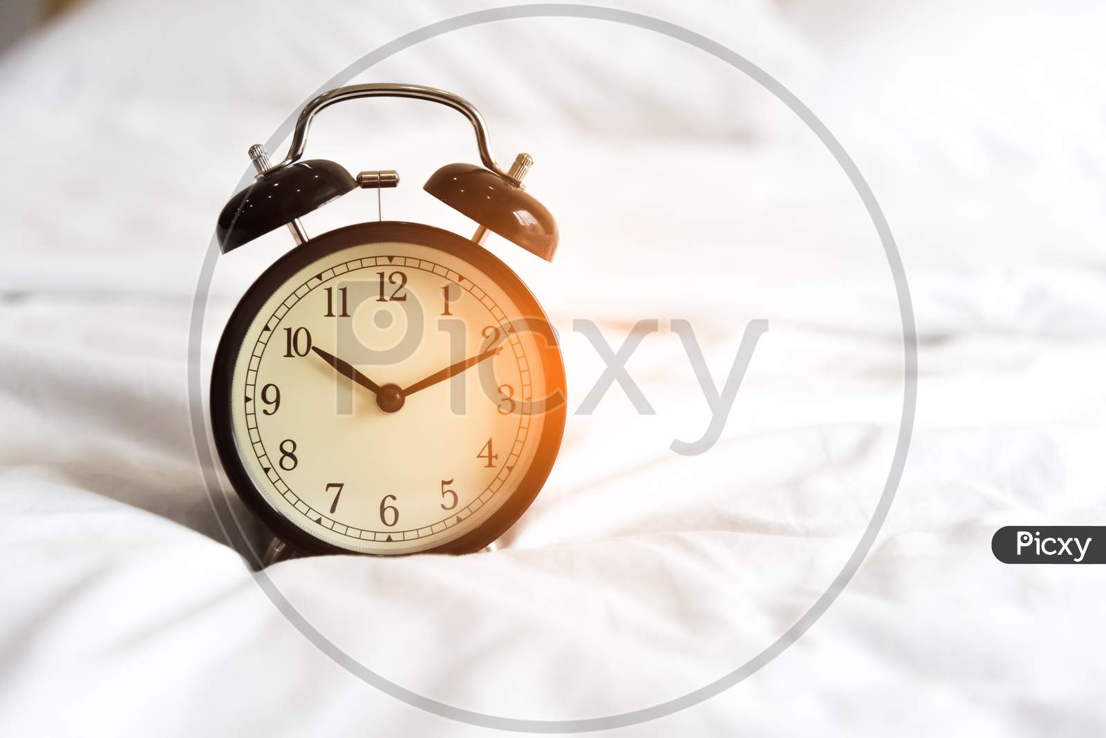 Alarm Clock On The White Bed. Holiday And Reminder Concept. Clock Hand Point To 10 O'Clock 10 Minute Time
