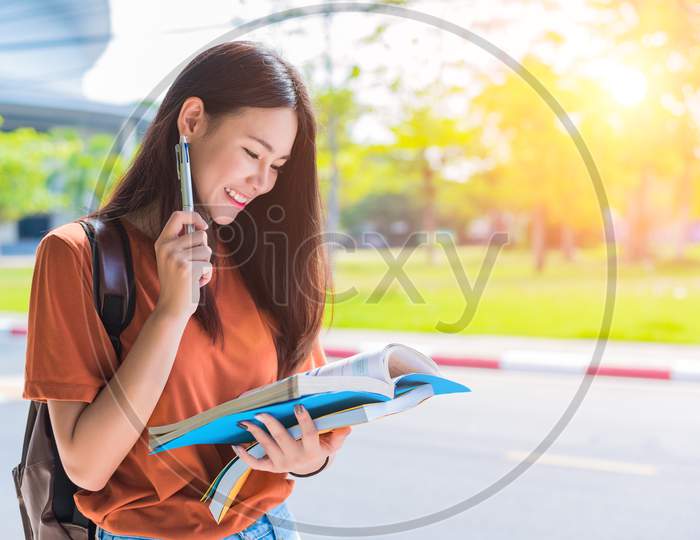 Asian Young College Woman Doing Homework And Reading Books For Final Examination In Campus. University And Student Concept. Lifestyle And Beauty Concept. Teenager And Learning Theme.
