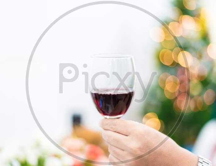 Glass Of Red Wine For Toasting In Party With Christmas Tree Background. Celebration And Anniversary Concept. New Year Toast And Drinking Concept.