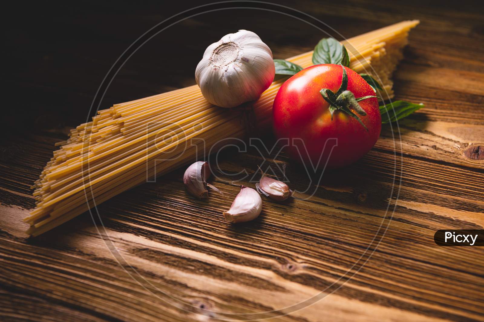 Tasty Appetizing Italian Spaghetti Pasta Ingredients For Kitchen Cuisine With Tomato, Garlic And Basil On Wooden Brown Table. Food Meal And Italian Recipe Homemade. Top View Abgle Above