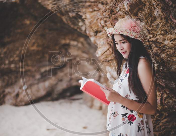Beauty Asian Woman Reading Book At Beach. Lifestyles And Nature Concept. Relaxation And Leisure Concept. Summer And Tropical Theme.