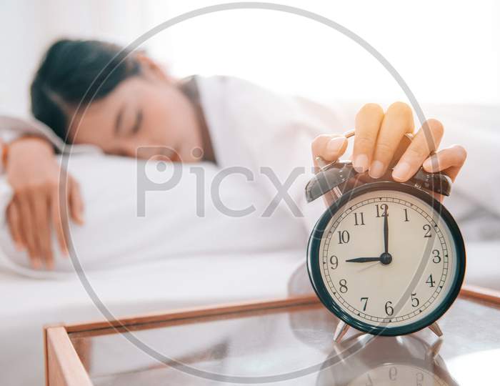 Asian Young Beauty Woman Turning Off Alarm Clock In Morning Without Looking. Lazy Time And Holiday Concept. Bedroom Theme.