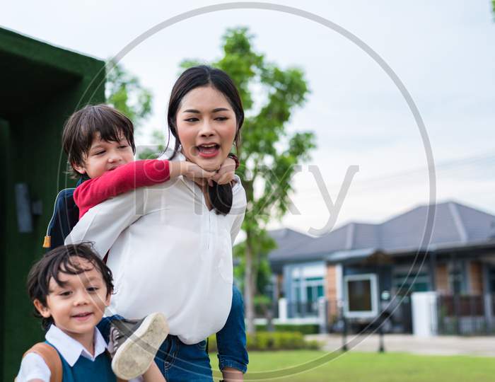 Single Mom Carrying And Playing With Her Children In  Garden With Green Wall Background. People And Lifestyles Concept. Happy Family And Home Sweet Home Theme. Outdoors And Nature Theme.