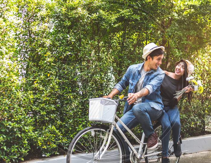 Happy Couple Riding Bicycle Together In Romantic View Park Background. Valentine'S Day And Wedding Honeymoon Concept. People And Lifestyles Concept.
