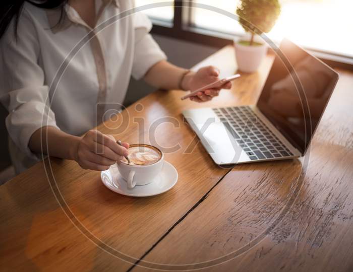Close Up Of Business Woman Working With Laptop And Drinking Coffee In Office. Business And Lifestyles Concept. Entrepreneur And Freelance Theme. Selective Focus On Coffee Cup