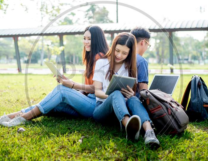 Group Of Asian College Student Using Tablet And Laptop On Grass Field At Outdoors. Technology And Education Learning Concept. Future Technology And Modern Entertainment Concept. Edutainment Theme.