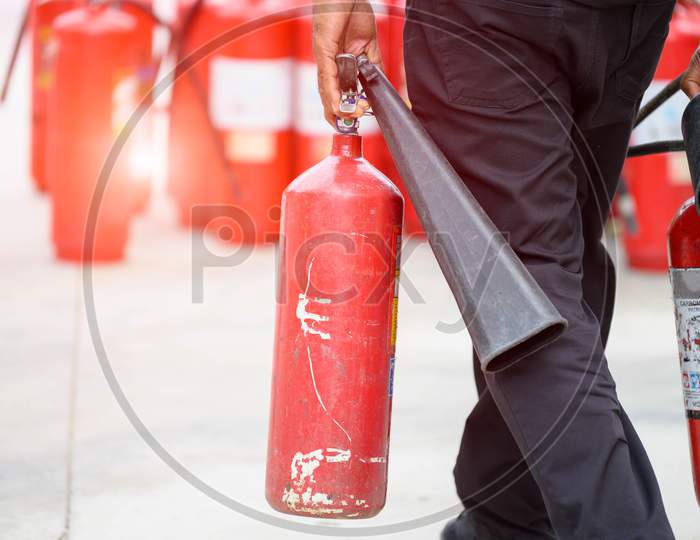 Closeup Of Fireman Lower Body Prepare To Fire Drill By Holding Portable Fire Extinguish And Water Hose. Security Insurance Protection And Fire Fighter Concept. Many Red Dry Chemical Tank Background.