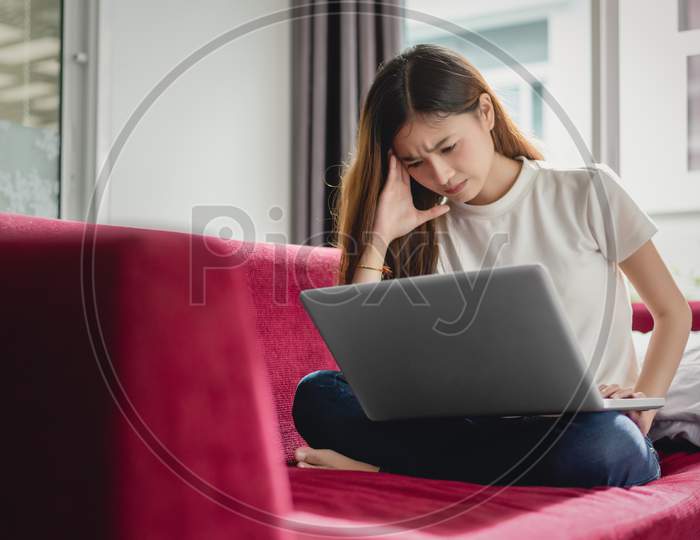 Exhausted Businesswoman Having A Headache While Using Laptop On Red Sofa, Business Worry And Stress Concept, Online Shopping And Marketing Concept.