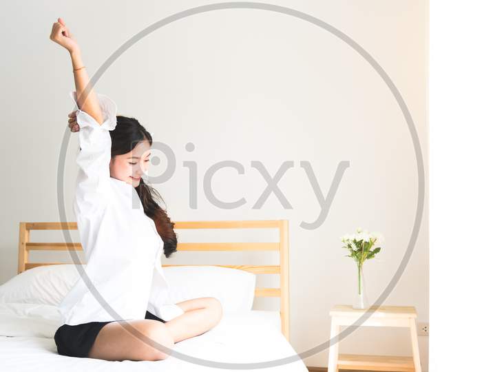 Rear View Of Woman Stretching In Morning After Waking Up On Bed Near Window. Holiday And Relax Concept. Lazy Day And Working Day Concept. Office Woman And Worker In Daily Life Theme